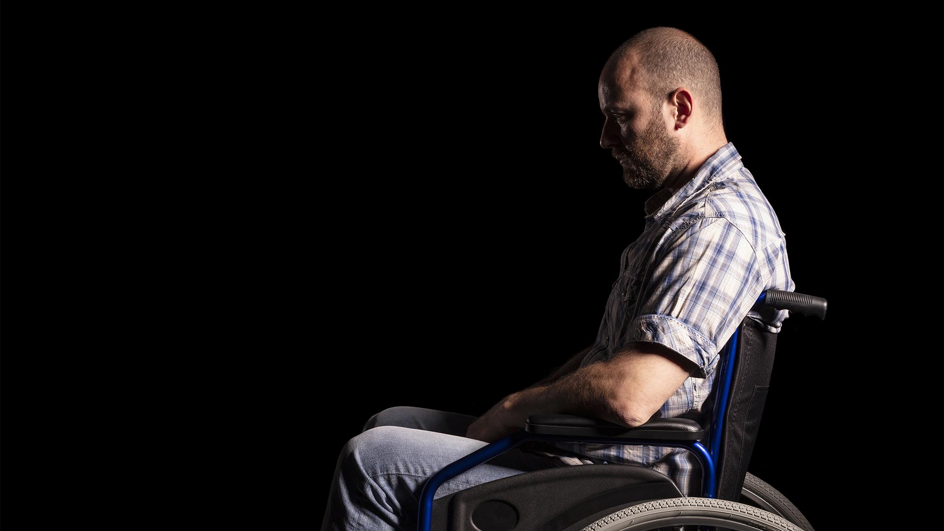 Man in wheelchair sits solemnly against black background to highlight the issue of ndis participant safety