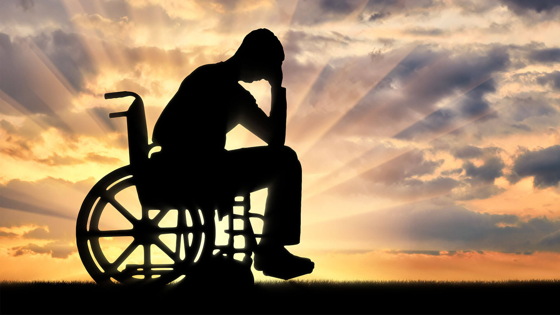 NDIS Participant Safety: Person in wheelchair silhoutted by sunrise bows with hand on head.