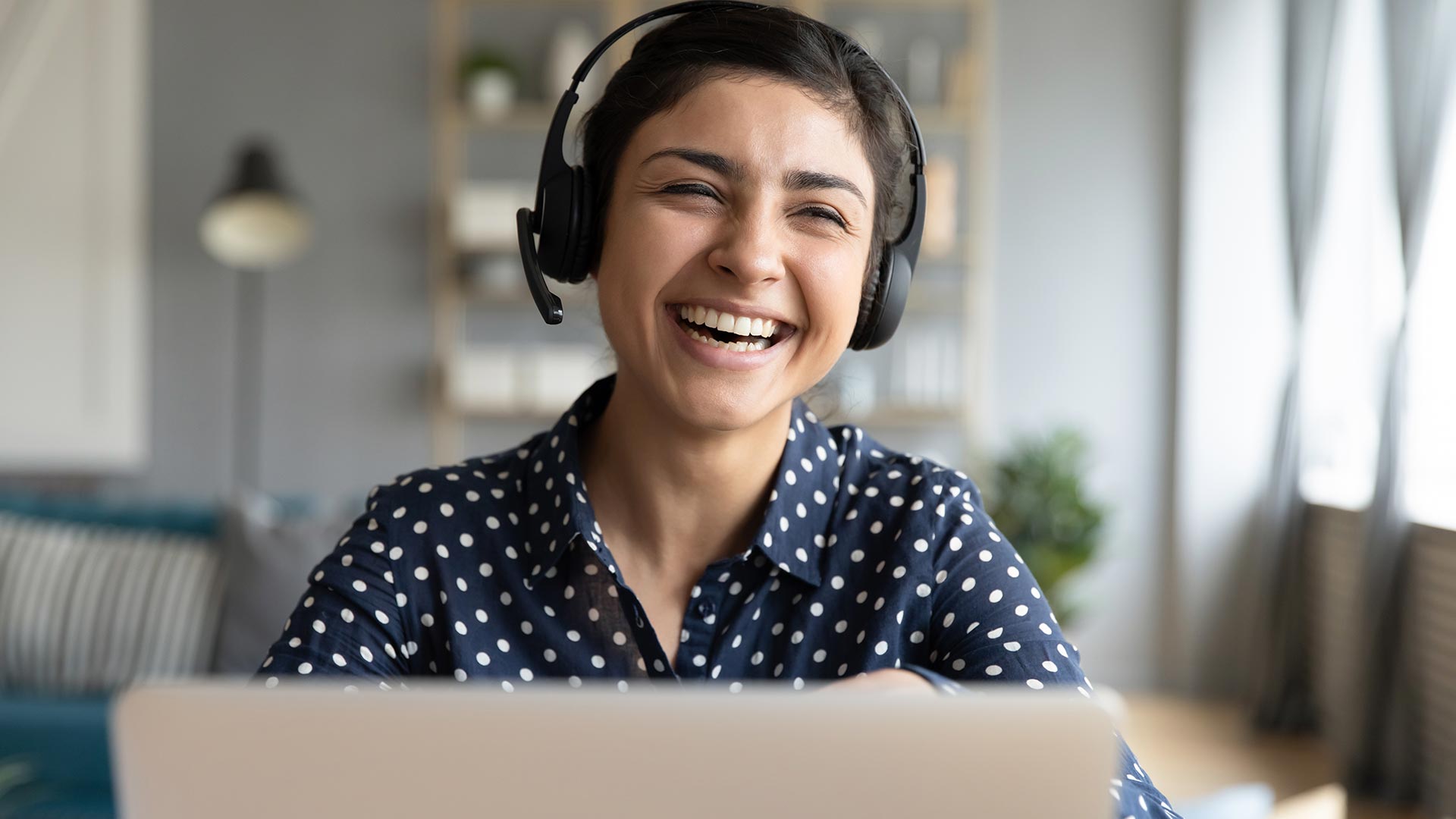 Young girl wearing headset sits laughing behind laptop screen