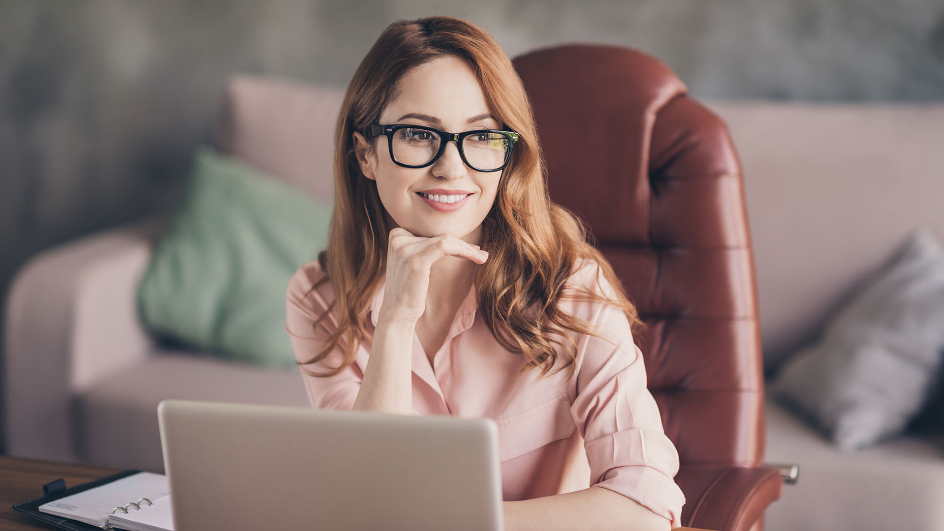 A young business woman sits smiling at her computer. Team building activities are an important part of building an inclusive and productive team culture
