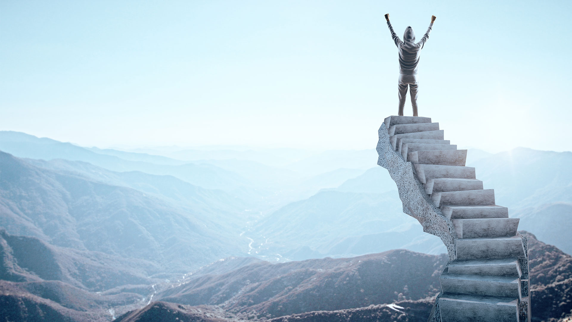 Amerginhub: The best is yet to come. A many stands atop a set of stairs facing out towards a mountain range with hands raised in success.